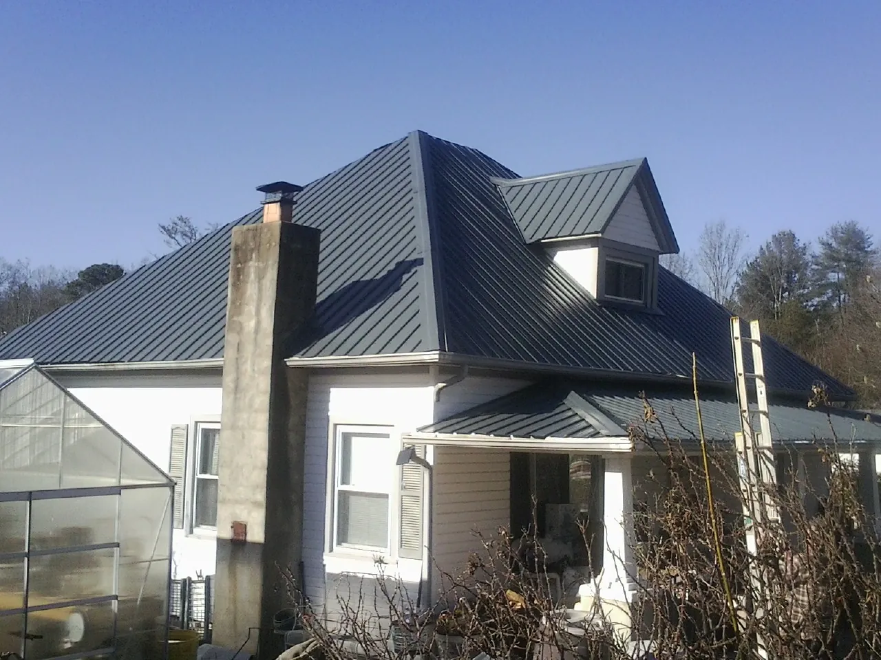 Dark blue standing seam metal roof on a white farmhouse with dormer — Slate & Tile Roof Repair by Roofing Brothers in Nolanville