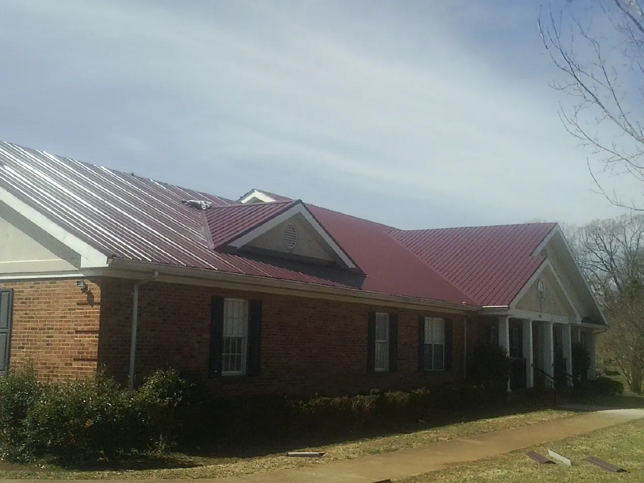 Red metal roof with gabled entries on a long brick building, from a Hail Damage Roof Repair job in Nolanville