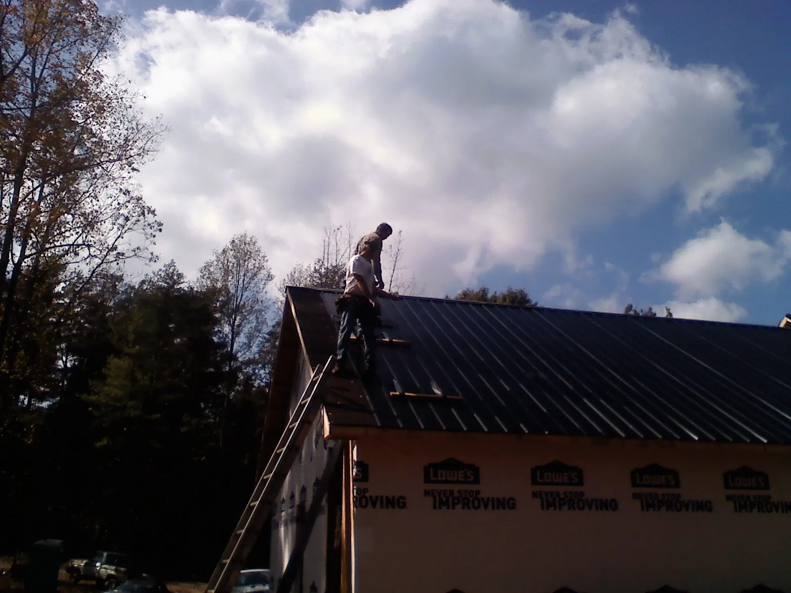 Roofer fastening dark metal panels high against a cloudy sky, from a Roof Inspection job in Nolanville
