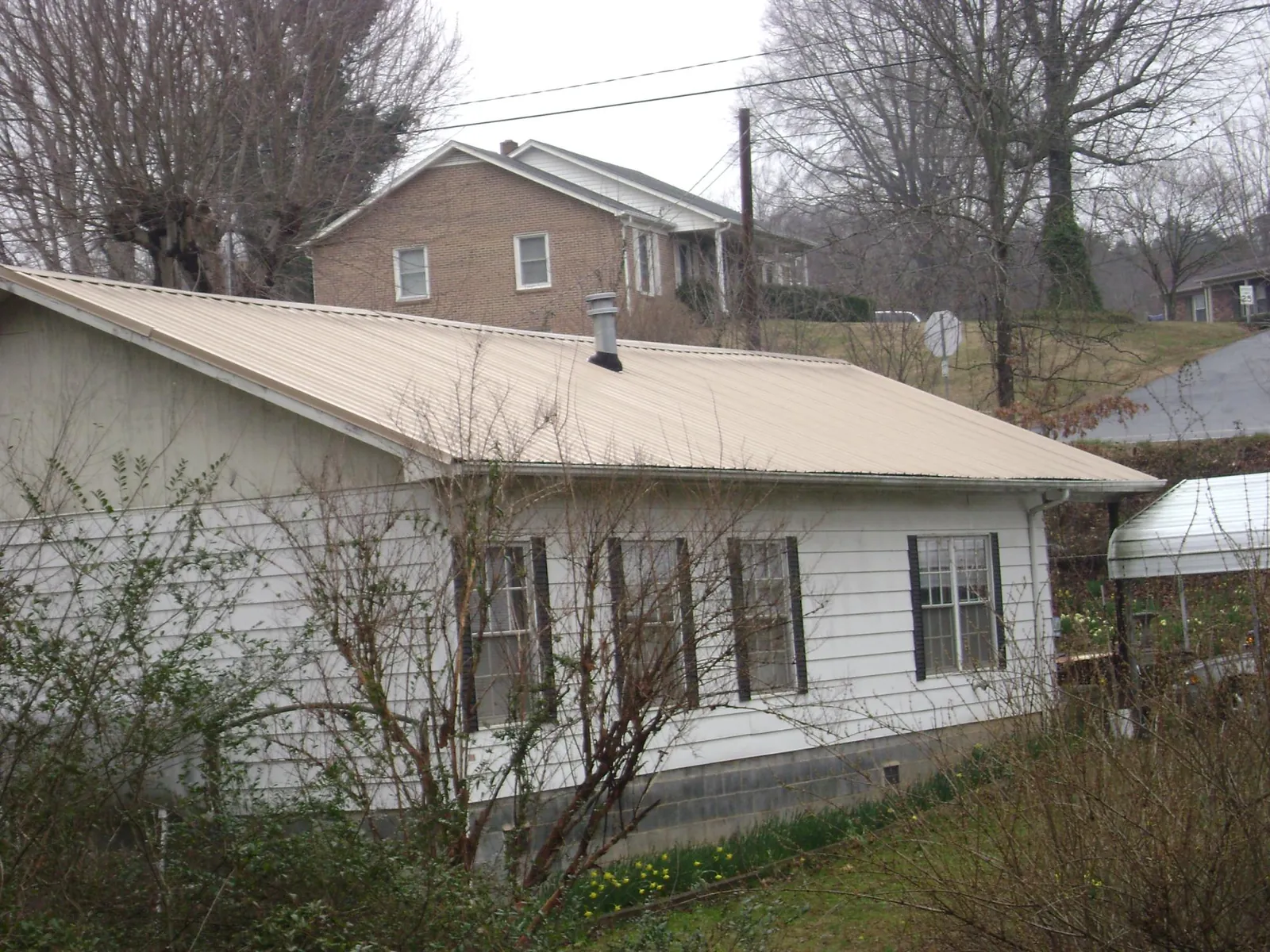 Tan metal roof on a white sided house set into a hillside — Commercial Roofing by Roofing Brothers in Nolanville